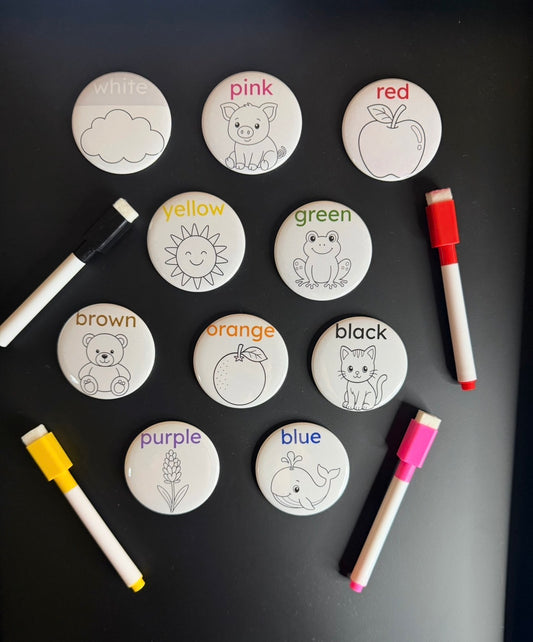 Ten round color-word magnets with outlined illustrations and dry erase markers on a dark surface